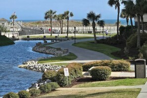 A coastal walkway with a bridge, palm trees, and a body of water. - Ocean Creek Lodge IV - 2287 (Myrtle Beach)
