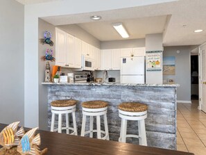 Une cuisine avec des meubles blancs, un réfrigérateur blanc et un îlot central en bois doté de tabourets.