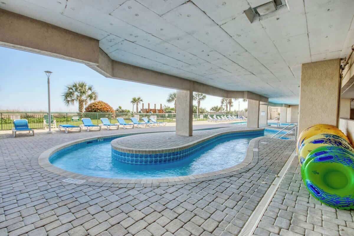 Un área de piscina con diseño curvo, sillas de descanso y vistas a la playa.