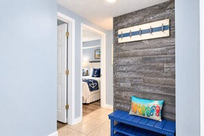 Een hal met een houten wand, een bankje en een deur naar een slaapkamer.