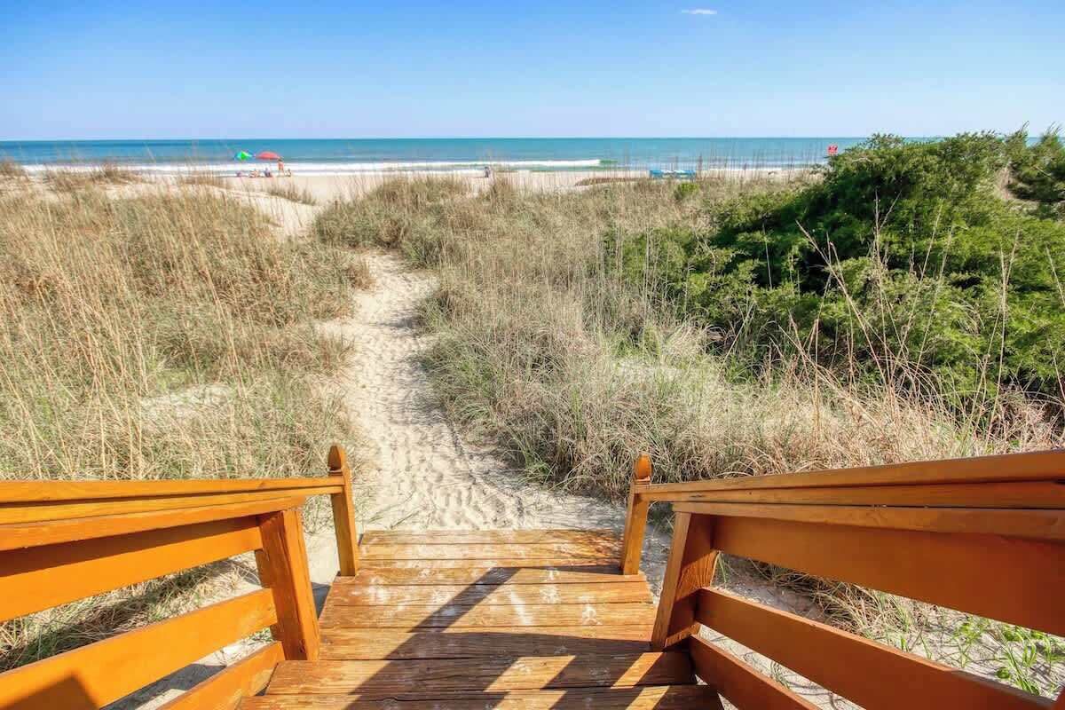A wooden pathway leading to beachside seating with a view of the ocean.