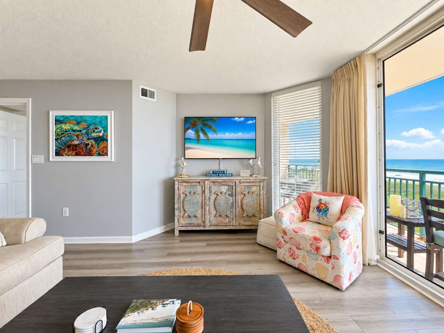 A living room with a sofa, a coffee table, a TV, and a cabinet. There is a view of the ocean through the window.