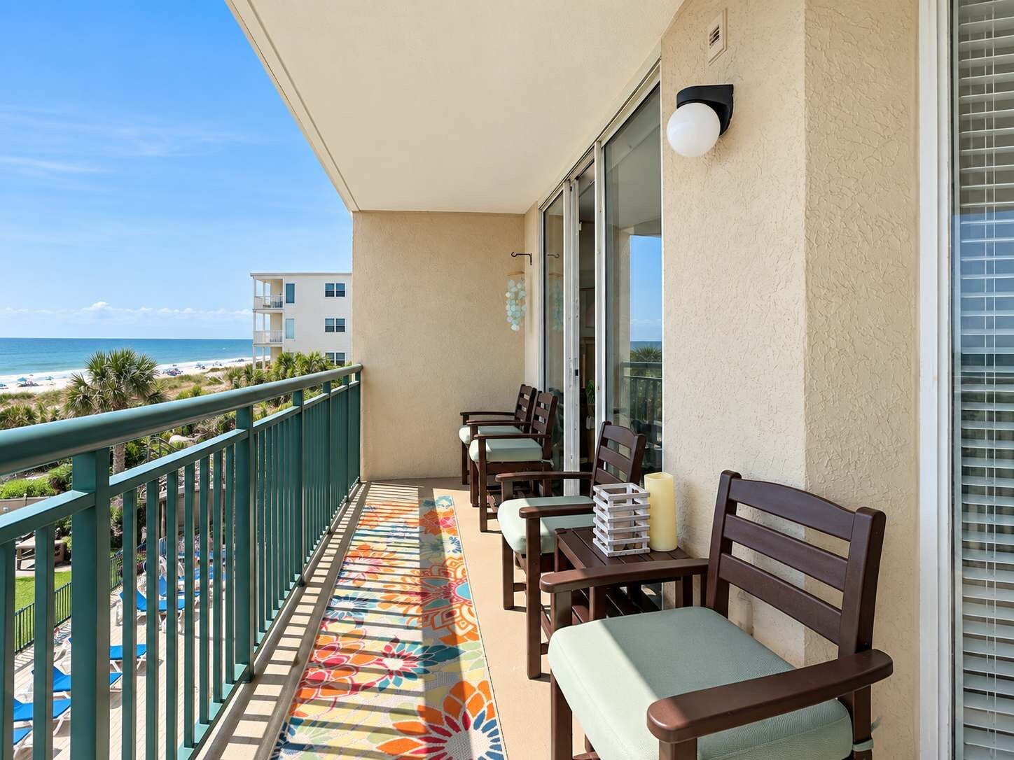 A balcony with a view of the beach, a table with chairs, and a railing.