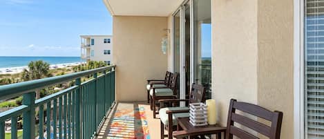 A balcony with a view of the beach, a table with chairs, and a railing.