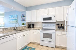 A kitchen with white cabinets, a microwave, an oven, a coffee maker, and a sign on the countertop. - Windy Hill Dunes 204 (North Myrtle Beach)
