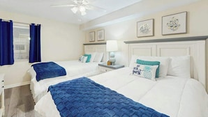 A hotel room with two beds, a ceiling fan, a window with curtains, and wall art. - Windy Hill Dunes 204 (North Myrtle Beach)