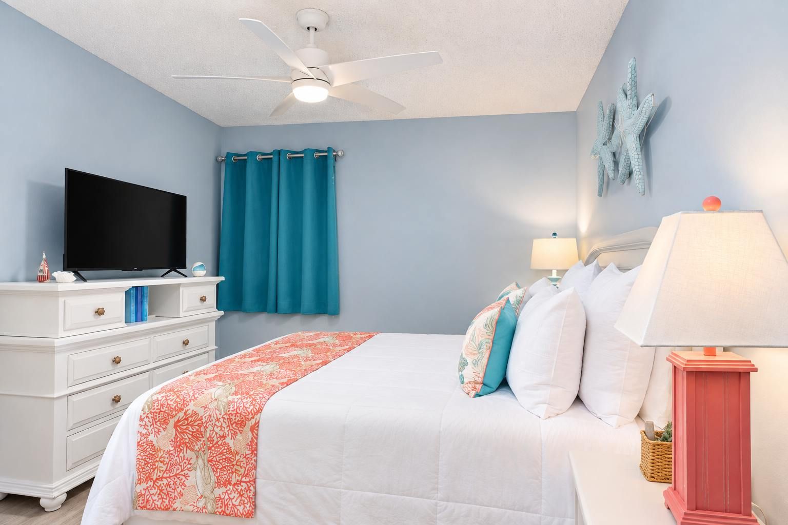 A bedroom with a bed, a television, a ceiling fan, and a starfish decoration on the wall.
