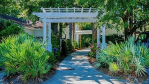 A pathway leading through a garden with a white pergola structure. - Marsh Hawk 3D at Litchfield by the Sea (Pawleys Island)