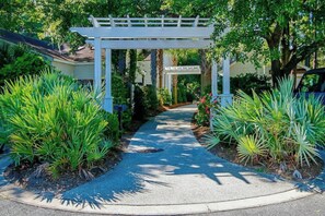 A pathway leading through a garden with a white pergola structure. - Marsh Hawk 3D at Litchfield by the Sea (Pawleys Island)