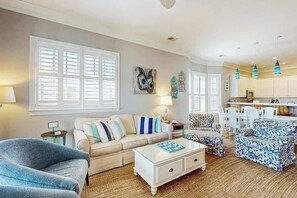 A living room with a sofa, armchair, and coffee table, a dining area with chairs, and a kitchen with cabinets and a microwave. - Marsh Hawk 3D at Litchfield by the Sea (Pawleys Island)