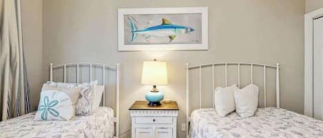 A bedroom with two beds, a nightstand with a lamp, and a wall-mounted painting of a fish.