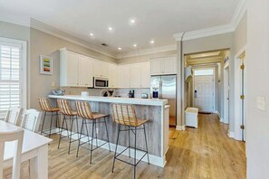 A modern kitchen with white cabinets, a central island with bar stools, and a refrigerator. - Marsh Hawk 3D at Litchfield by the Sea (Pawleys Island)