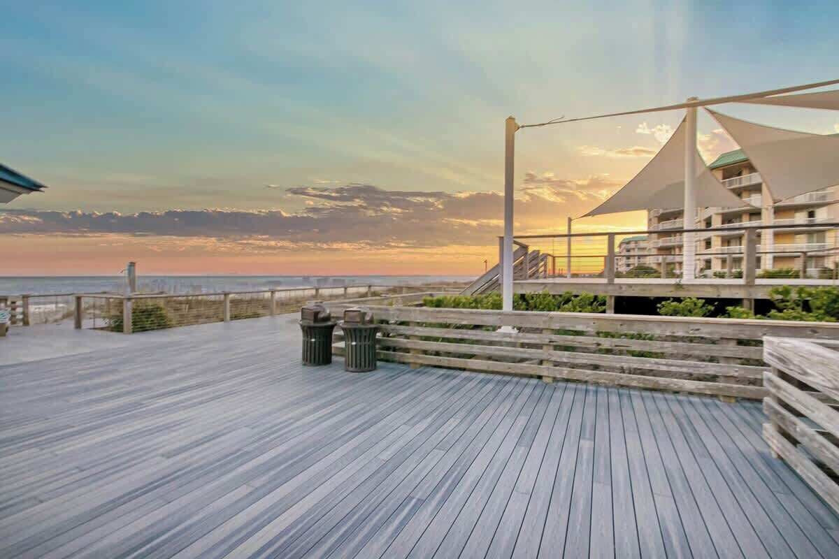 A wooden deck with a view of the ocean and a building with balconies.