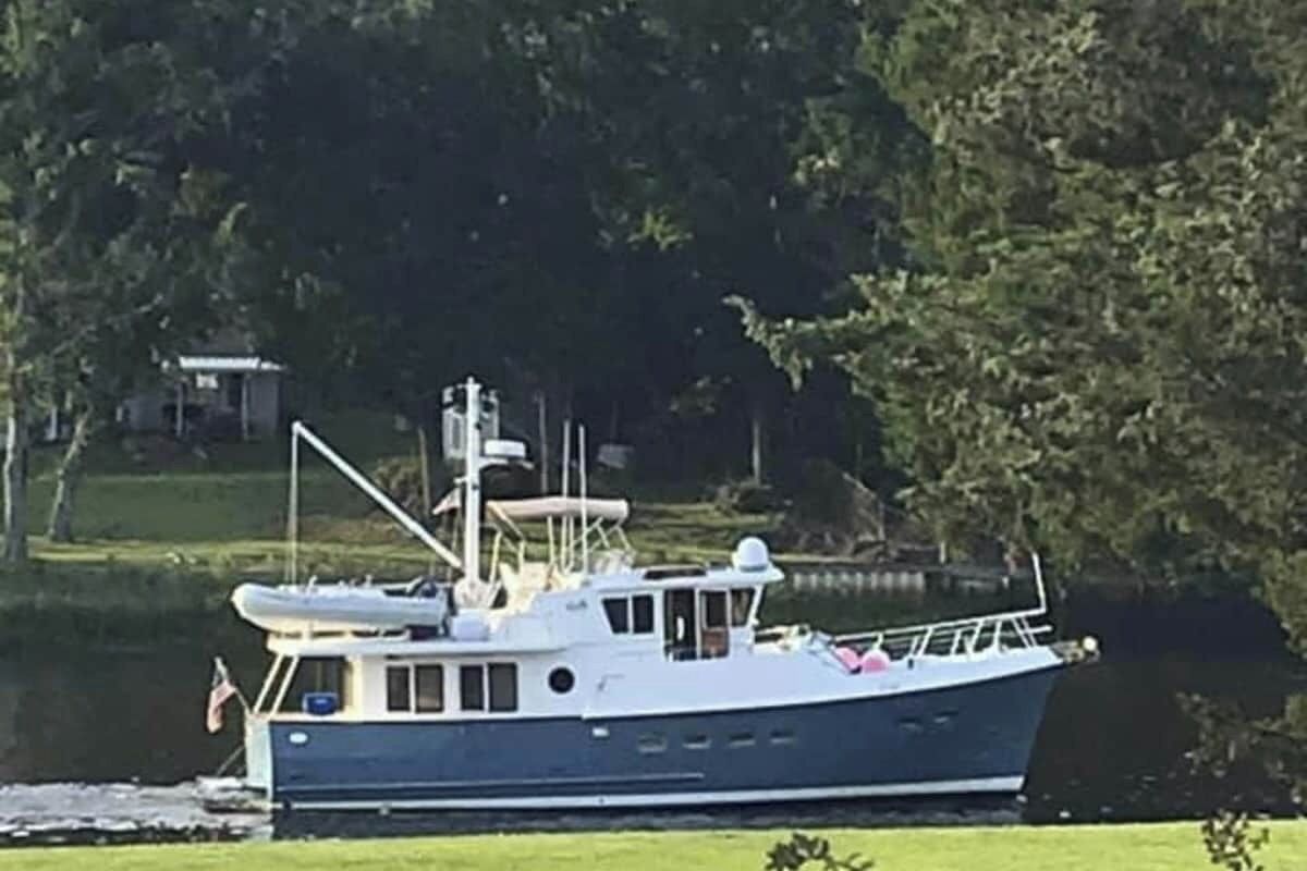 A boat docked near a grassy area with trees in the background.