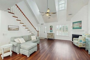 A spacious living room with a wooden staircase, a fireplace, and a ceiling fan. - Livin' the Dream at 26th Ave N (North Myrtle Beach)