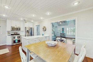A modern kitchen with white cabinetry, stainless steel appliances, and a wooden dining table. - Livin' the Dream at 26th Ave N (North Myrtle Beach)