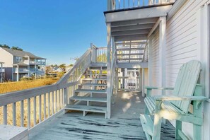 A wooden deck with a staircase leading to a covered area, a bench, and a view of neighboring buildings. - Livin' the Dream at 26th Ave N (North Myrtle Beach)
