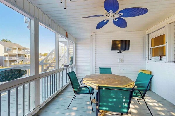 A covered outdoor area with a table and chairs, a ceiling fan, and a television mounted on the wall. - Livin' the Dream at 26th Ave N (North Myrtle Beach)