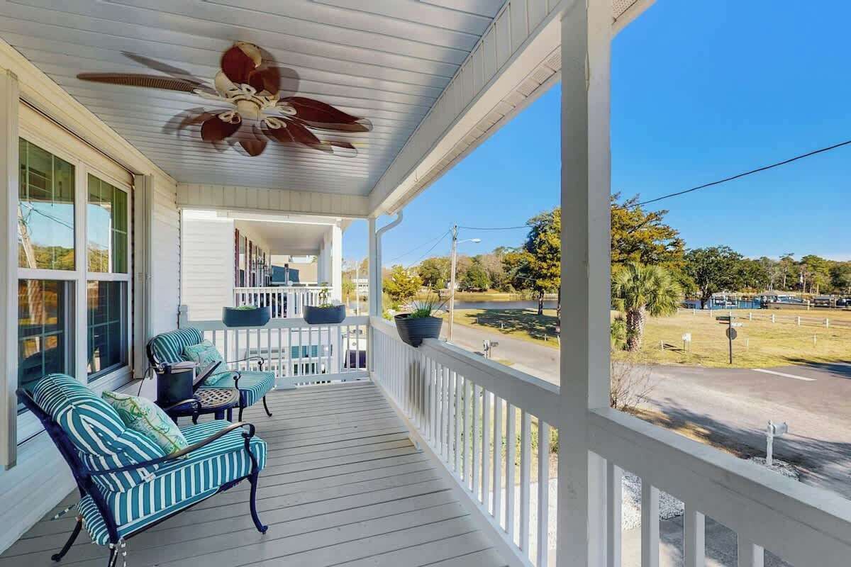 A covered porch with a ceiling fan, outdoor seating, and potted plants.