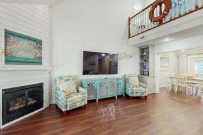 A spacious living room with a fireplace, a television, and a dining area with a staircase. - Livin' the Dream at 26th Ave N (North Myrtle Beach)