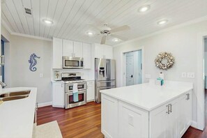 A modern kitchen with white cabinetry, stainless steel appliances, and a large island. - Livin' the Dream at 26th Ave N (North Myrtle Beach)