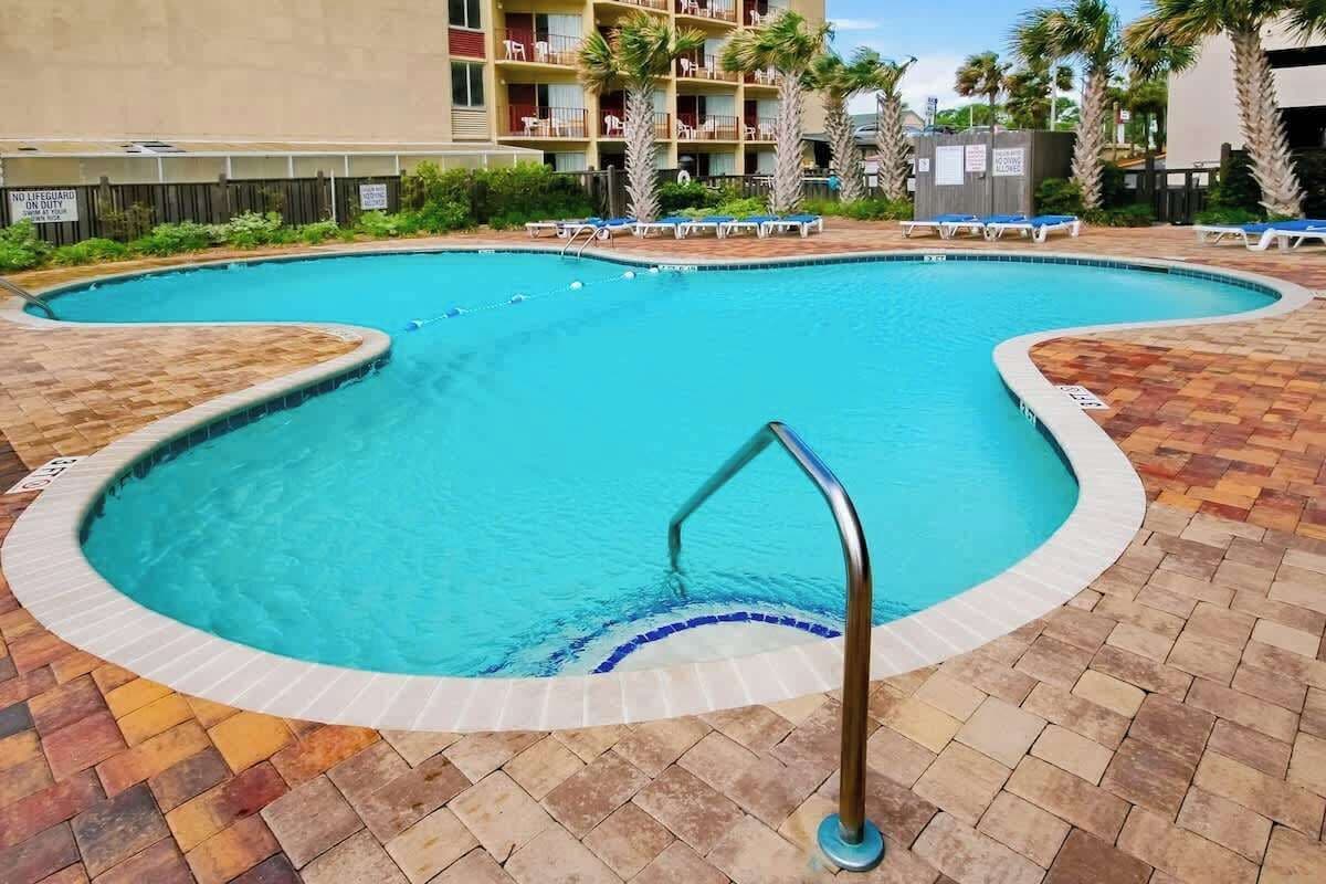 Piscina com borda curva, rodeada por espreguiçadeiras e um deck revestido de azulejos.