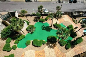 Eine Luftaufnahme einer angelegten Grünfläche mit Palmen, einem Wasserspielplatz und einem Parkplatz.