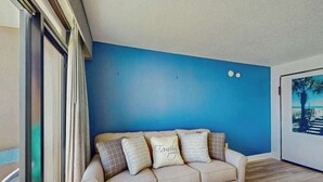 Et værelse med en blå væg, en beige sofa med mønstrede puder og et billede i ramme på væggen.