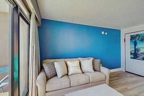 Ein Zimmer mit blauer Wand, einem beigen Sofa mit gemusterten Kissen und einem gerahmten Bild an der Wand.