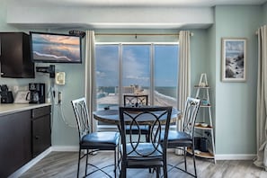 A room with a dining table, chairs, a television, a coffee machine, and a view of the beach. - Palace Resort Unit 1604 (Myrtle Beach)