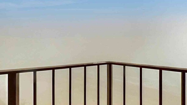 Un balcon avec une balustrade en métal et un ciel dégagé en arrière-plan.