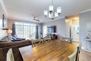 A dining area with a wooden table and chairs, a sofa, a ceiling fan, and a chandelier. - Wedgewood Unit 423 Condo (North Myrtle Beach)