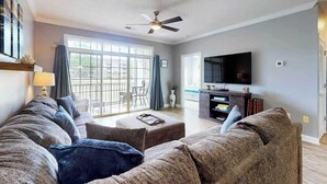 A living room with a sofa set, a television, and a ceiling fan. - Wedgewood Unit 423 Condo (North Myrtle Beach)