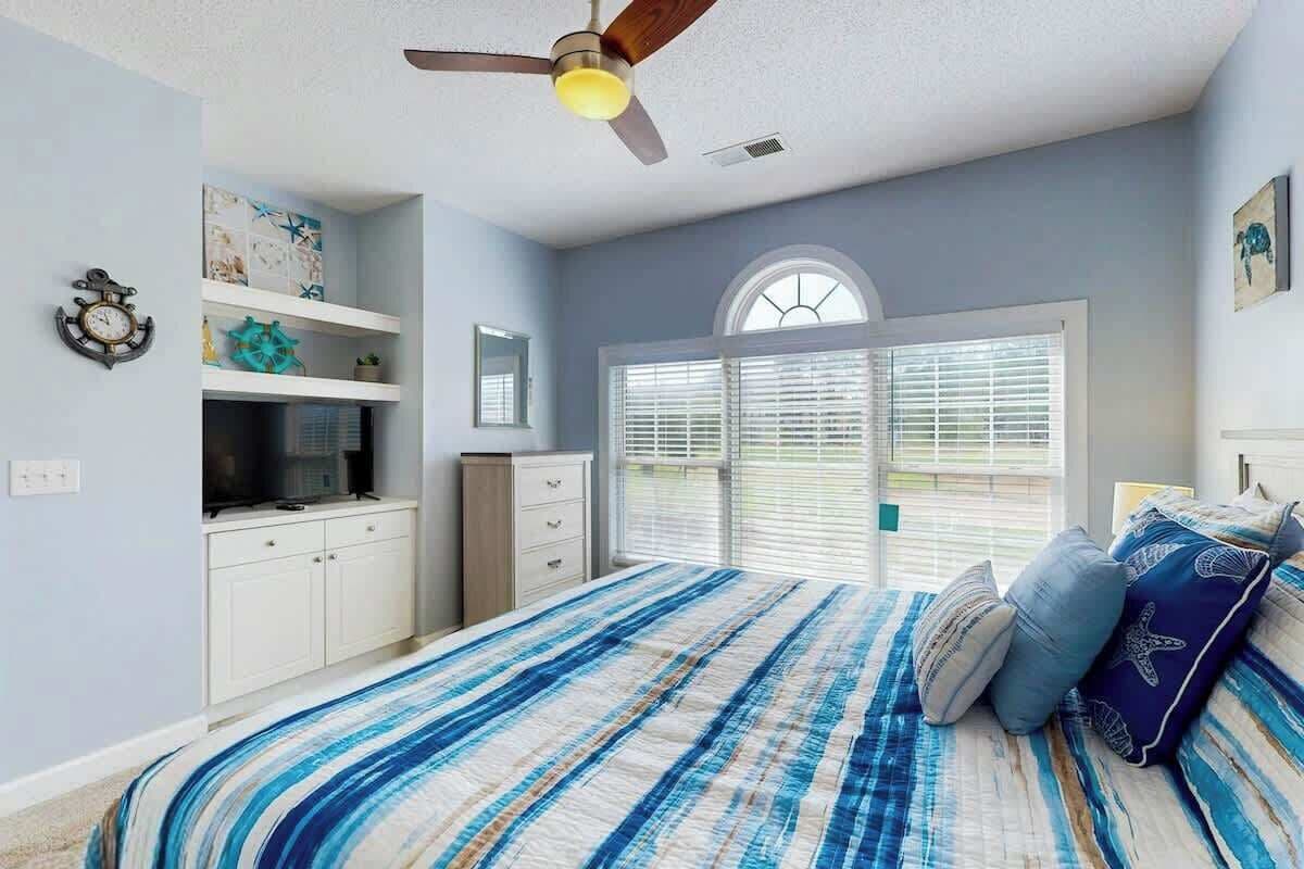 Ein Schlafzimmer mit einem Bett, einem Deckenventilator, einem Fenster mit Jalousien und einem Wandregal mit Dekoration.