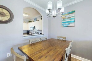 A dining area with a wooden table and chairs, a kitchen visible through an archway, and a wall clock. - Wedgewood Unit 423 Condo (North Myrtle Beach)