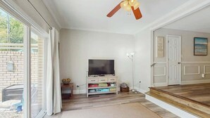 Een woonkamer met een televisie, een plafondventilator en een schuifdeur naar een buitenruimte.