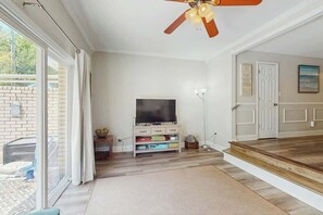 A living room with a television, a ceiling fan, and a sliding glass door leading to an outdoor area. - Beach Life Retreat Home (Myrtle Beach)