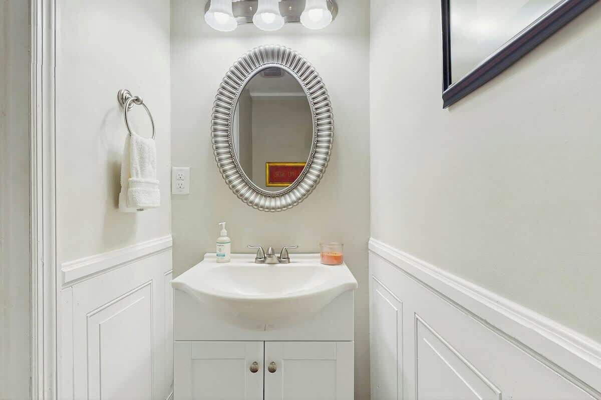 A bathroom with a white vanity, a mirror with a decorative frame, a towel ring, a sink with a soap dispenser, and a candle.