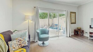Een woonkamer met een bank, een blauwe fauteuil, een tv-meubel en een schuifpui naar een buitenruimte.