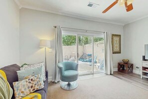 A living room with a sofa, a blue armchair, a TV stand, and a sliding glass door leading to an outdoor area. - Beach Life Retreat Home (Myrtle Beach)