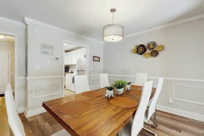 A dining area with a wooden table, white chairs, and a pendant light. - Beach Life Retreat Home (Myrtle Beach)
