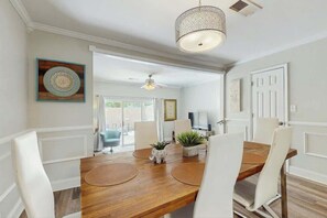 A dining area with a wooden table, white chairs, a hanging light fixture, and a door leading to an outdoor space. - Beach Life Retreat Home (Myrtle Beach)