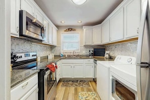 A compact kitchen with white cabinets, a built-in microwave, a stove, and a dishwasher. - Beach Life Retreat Home (Myrtle Beach)