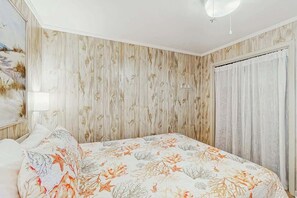 A bedroom with a bed, a nightstand, a wall with a floral pattern, and a window with curtains. - Ocean Pier IV Unit - 332 (North Myrtle Beach)