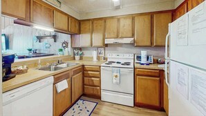 A kitchen with wooden cabinets, a white stove, a ceiling fan, and a refrigerator with papers on it. - Ocean Pier IV Unit - 332 (North Myrtle Beach)