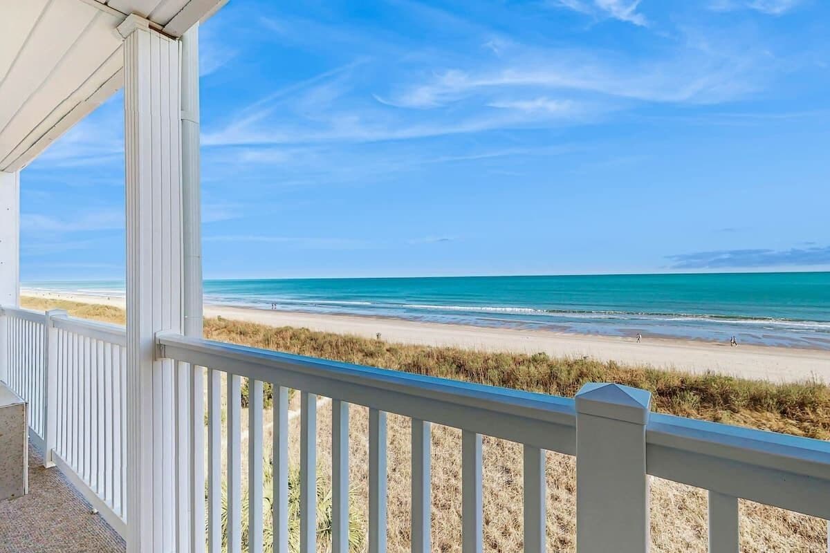 A beach view from a covered balcony with white railings.