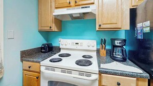 A kitchen with a white stove, wooden cabinets, and a black refrigerator. - The Arbor Unit 303 Condo (Myrtle Beach)