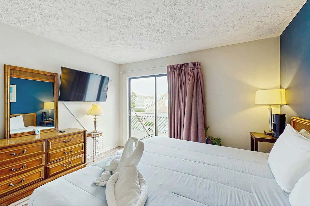 Una habitación de hotel con cama, televisión, cómoda y ventana con cortinas.