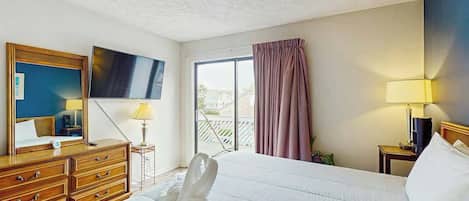 Una habitación de hotel con cama, televisión, cómoda y ventana con cortinas.