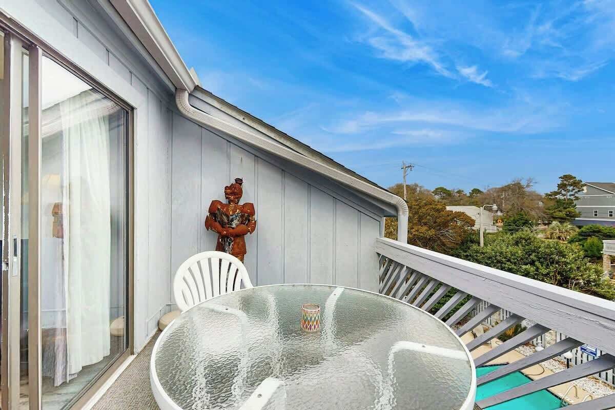 A balcony with a glass table and chairs, a statue, and a view of the neighborhood.